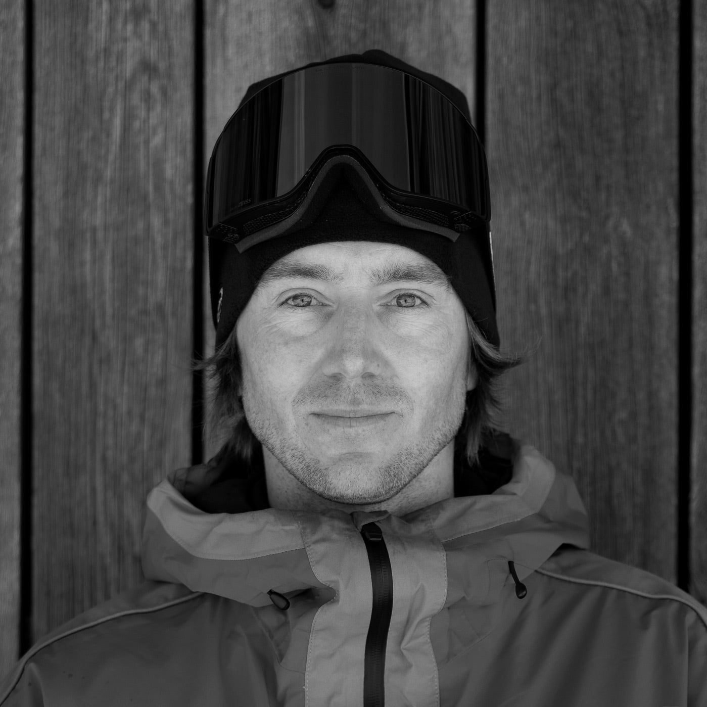 Werni wearing a hooded jacket and goggles against a wooden background